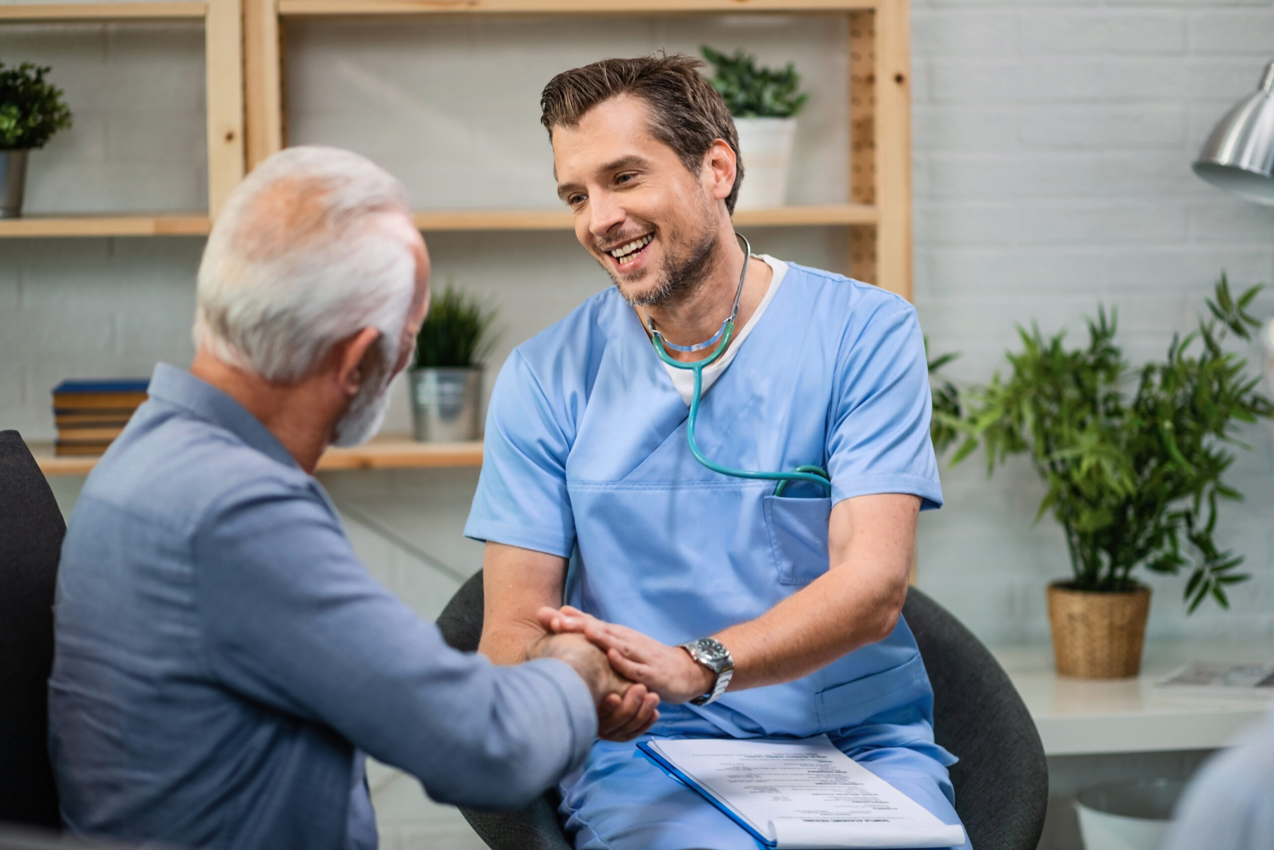 Happy general practitioner talking to senior man while shaking hands with him during a home visit.